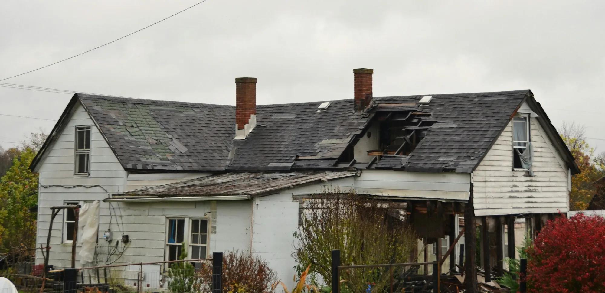 Old white farmhouse with a sagging, damaged shingle roof and two chimneys